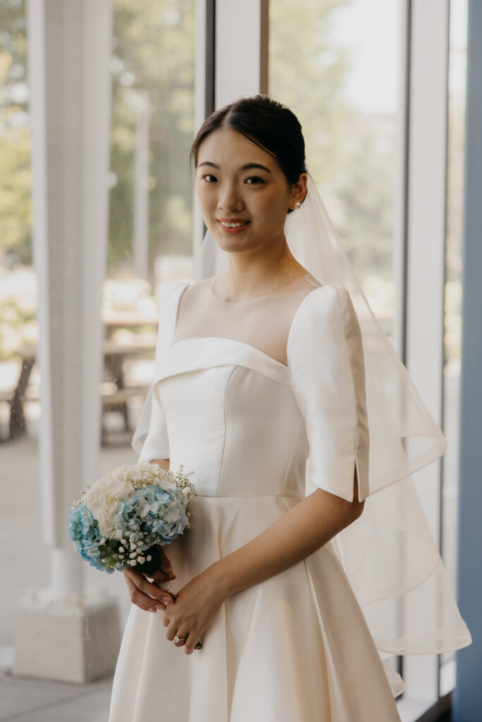 Bride smiles directly at the camera holding her blue and white hydrangea bouquet inside the American Swedish Institute