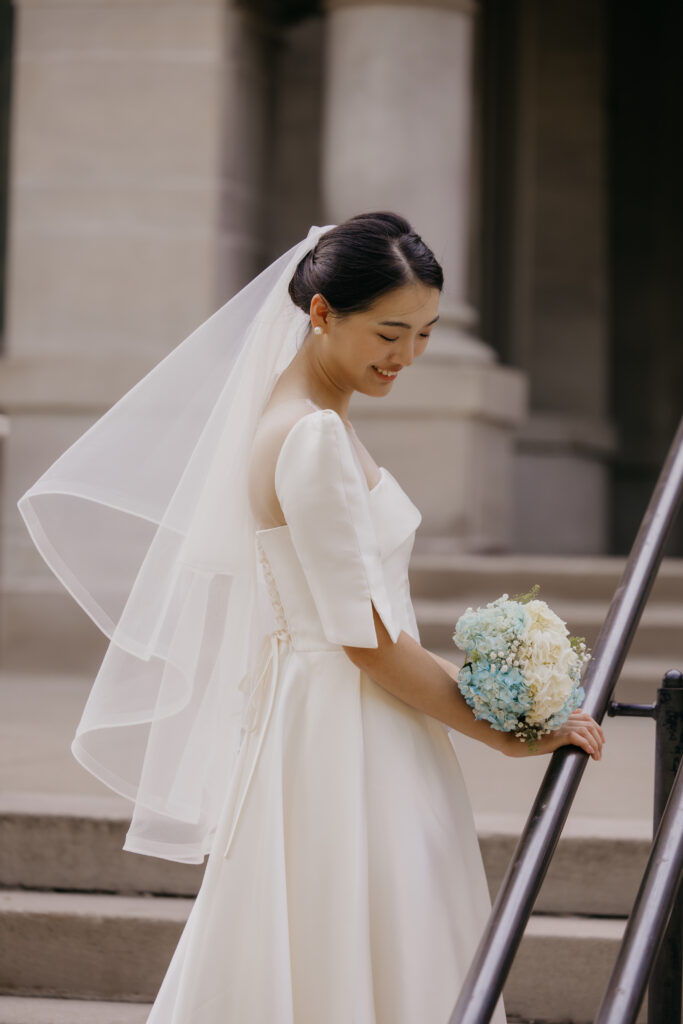 Bride looks down at her bouquet while walking down an outdoor staircase near Central Lutheran Church