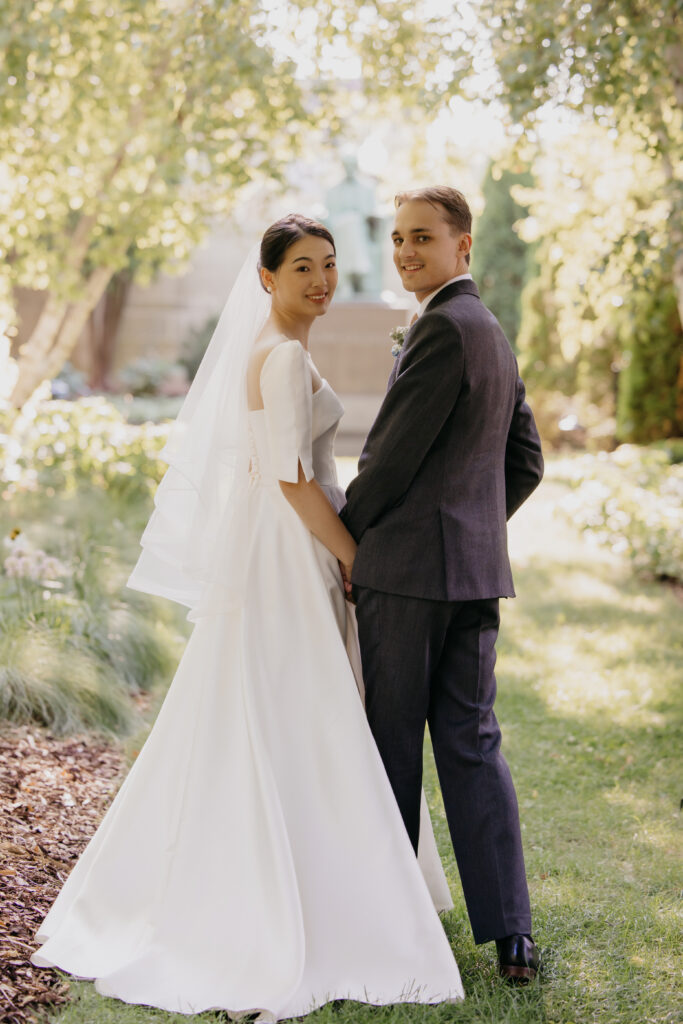 Bride and groom stand back to back holding hands in the American Swedish Institute garden