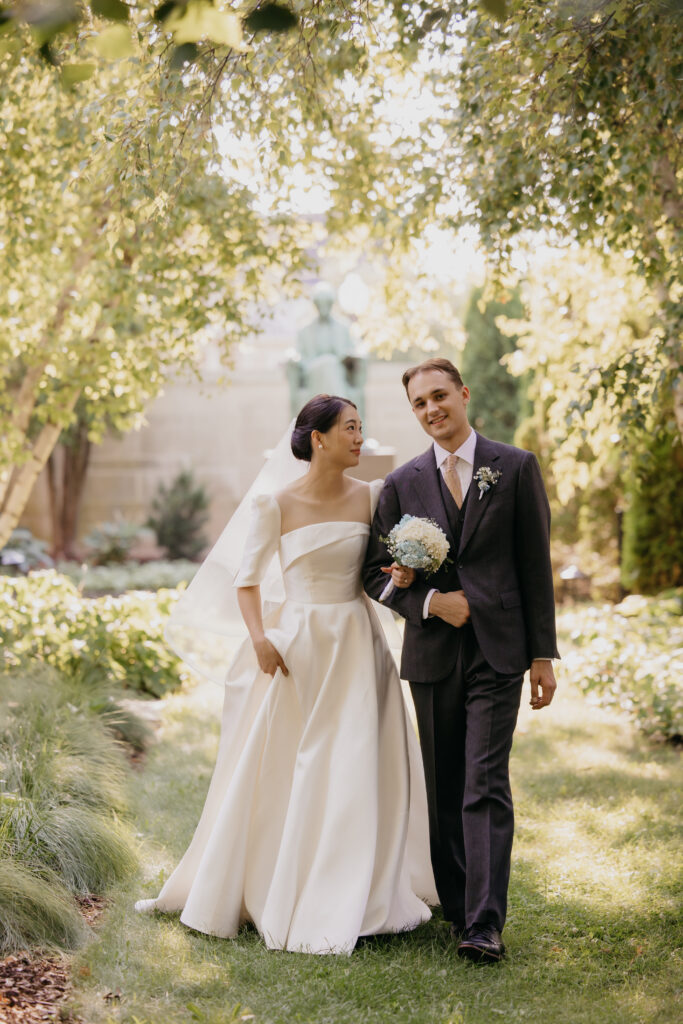 Bride and groom stand close together in front of a garden statue at the American Swedish Institute