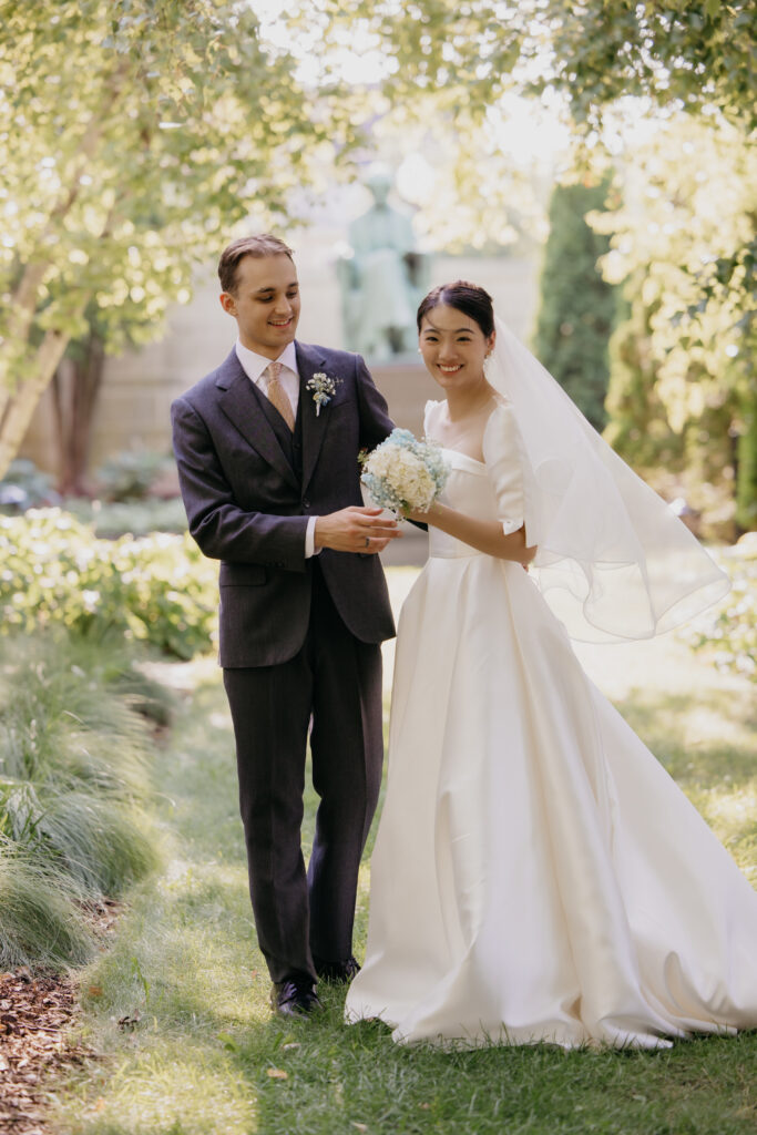 Groom walks hand in hand with bride past a garden statue at the American Swedish Institute