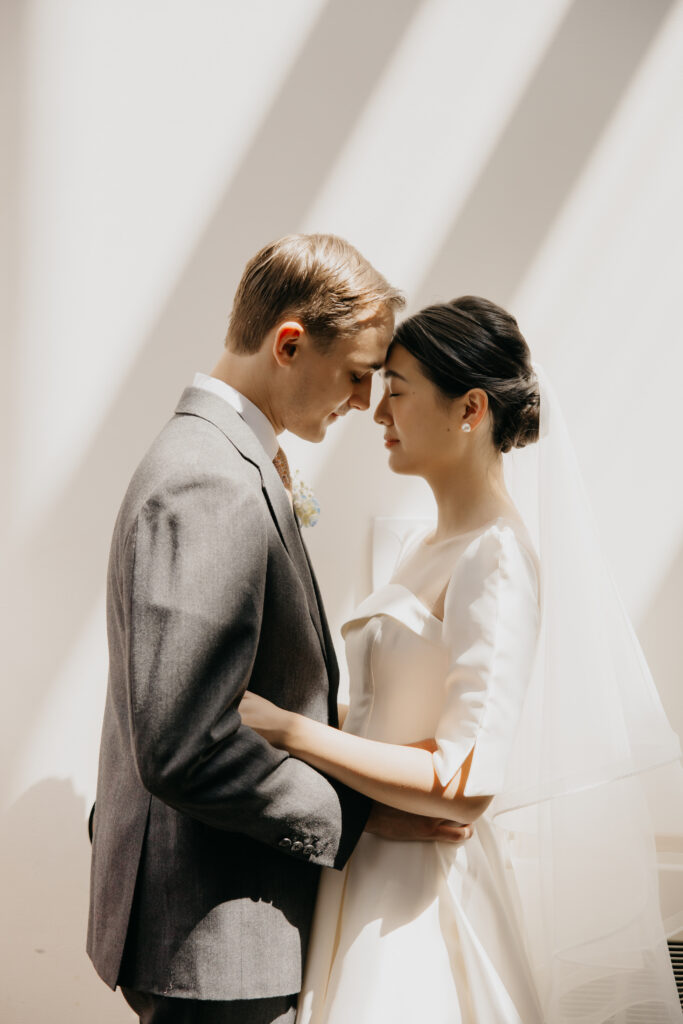 Groom and bride stand forehead to forehead in soft natural light inside the American Swedish Institute
