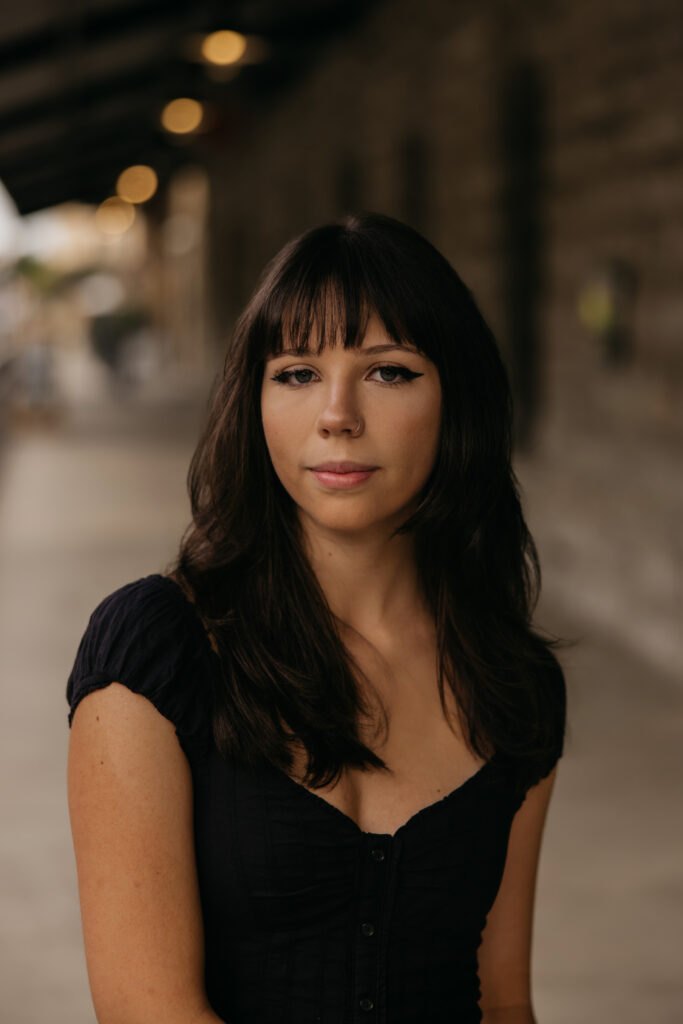 Senior close-up portrait with bangs in a black dress in a brick corridor