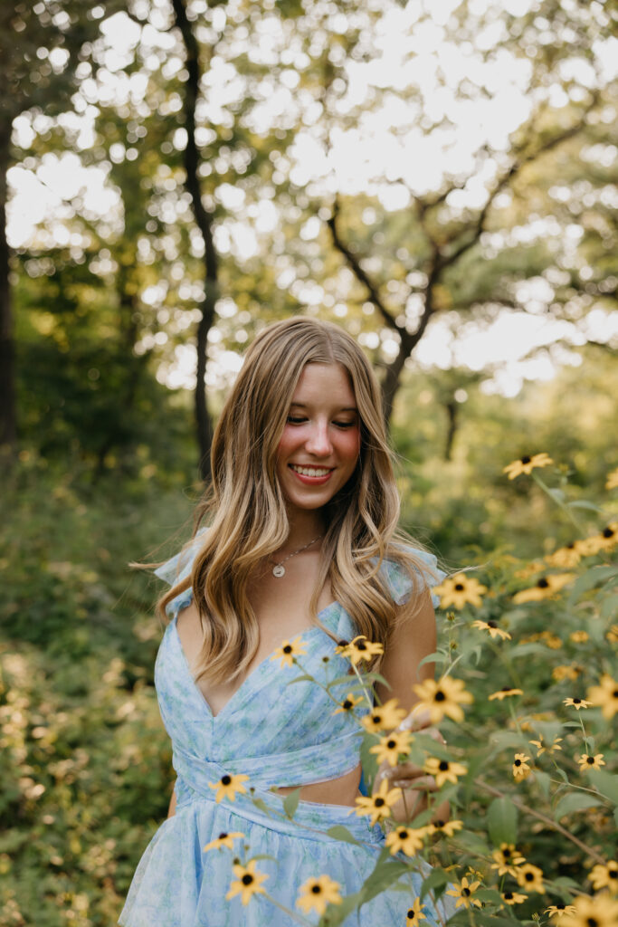 Senior smiling among black-eyed Susans in a blue ruffled dress