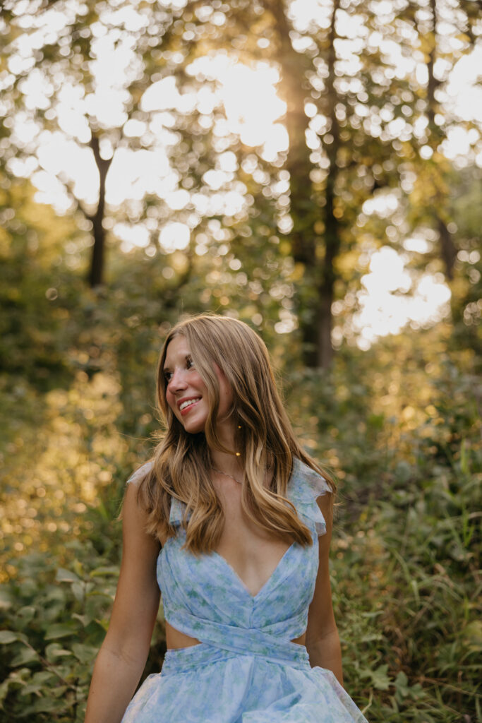 Senior in profile smiling in a blue floral dress with soft golden light behind her