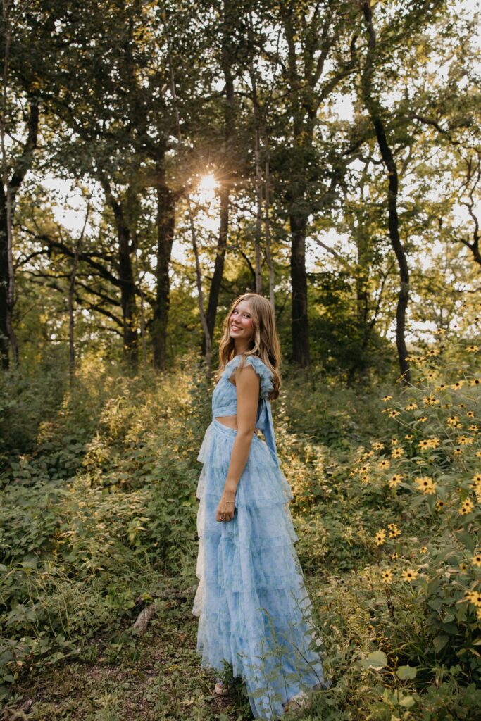 Senior standing among sunflowers and wildflowers in a blue ruffled dress