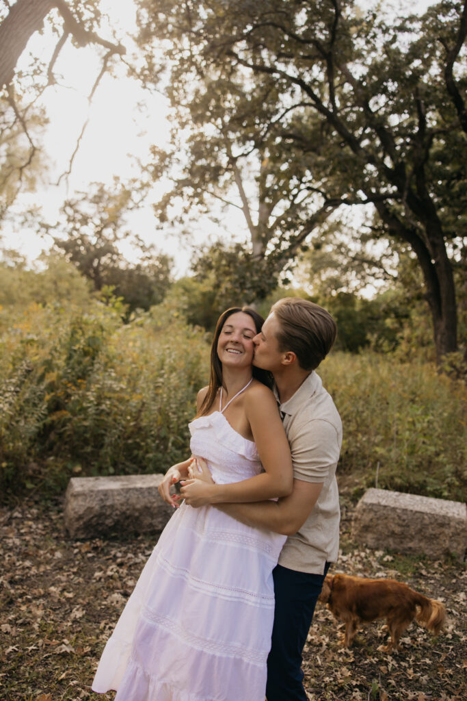 Couple hugging and smiling in a park with their small dog beside them