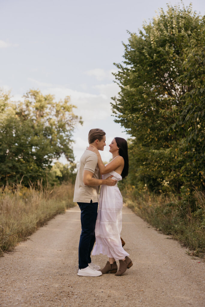 Couple embracing on a gravel path lined with trees during an evening engagement session