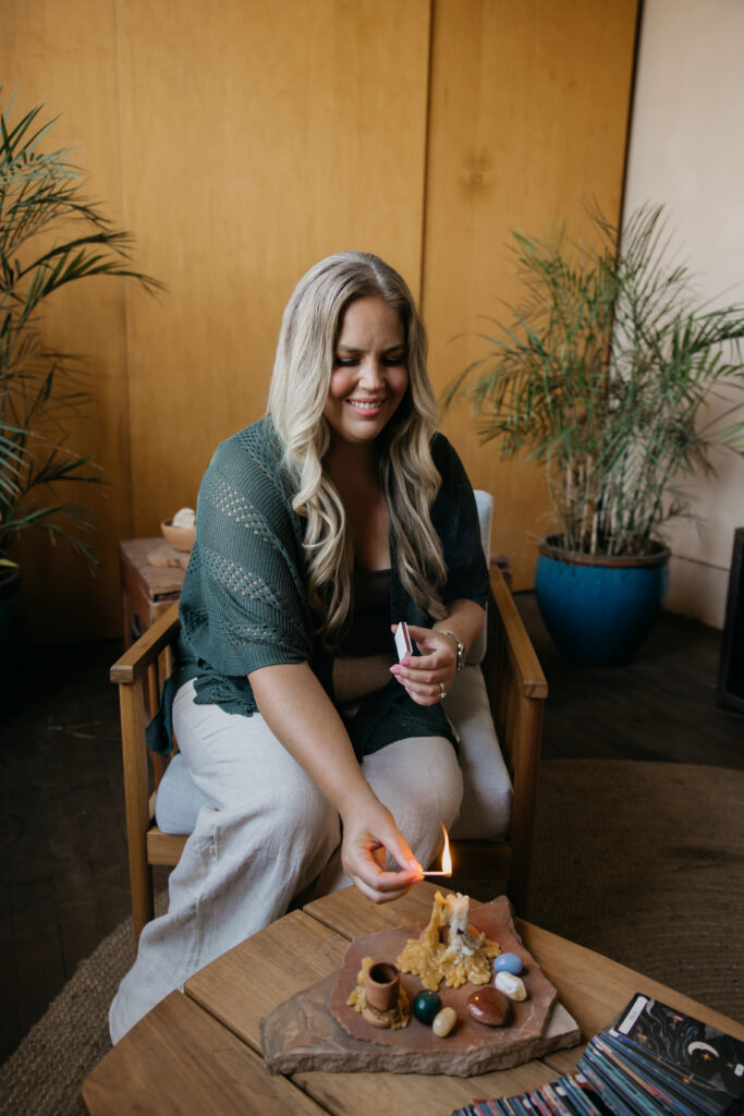 Caitlin Weseman lighting a candle beside crystals and cards on a wooden coffee table