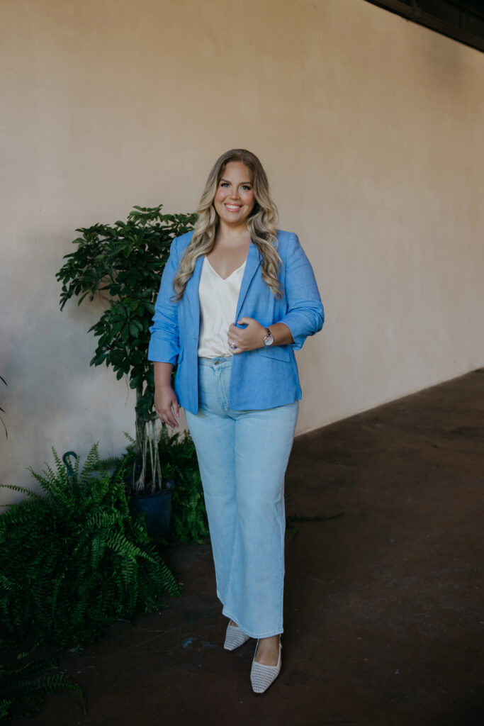 Full-length portrait of Caitlin Weseman in a blue blazer and light jeans among plants