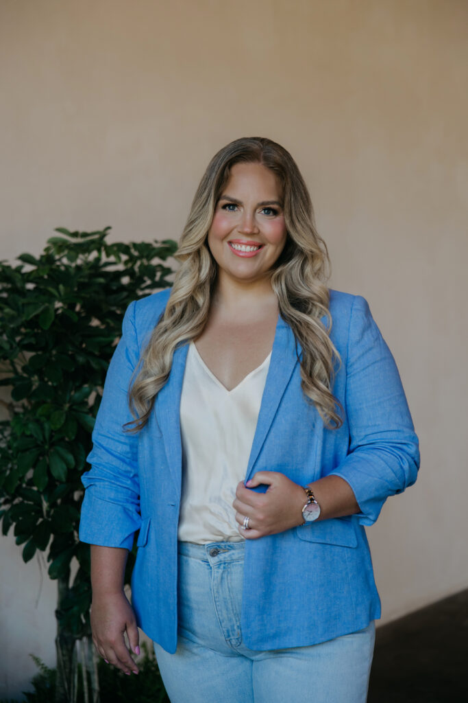 Astrologer Caitlin Weseman smiling in a blue linen blazer beside a leafy green plant