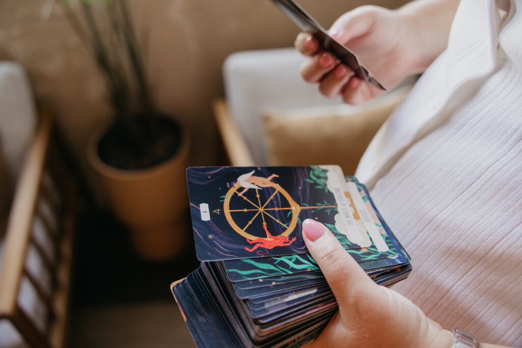 Hands holding a phone and a zodiac wheel card deck during an astrologer brand session