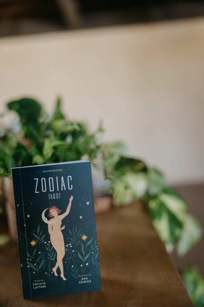 Zodiac Tarot book standing on a wooden table against trailing green plants