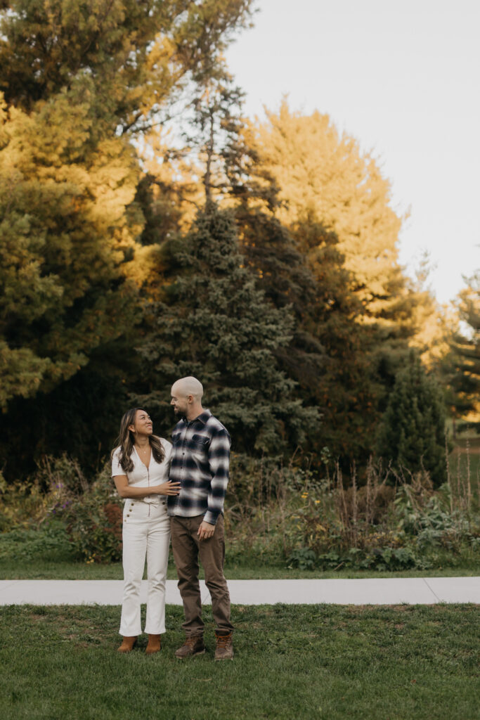 Couple standing together on a garden path with golden fall trees in the background