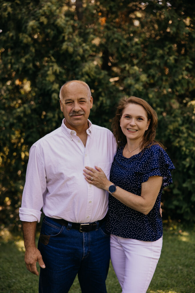 Grandparents smiling together in front of a tree line during a family reunion photography session