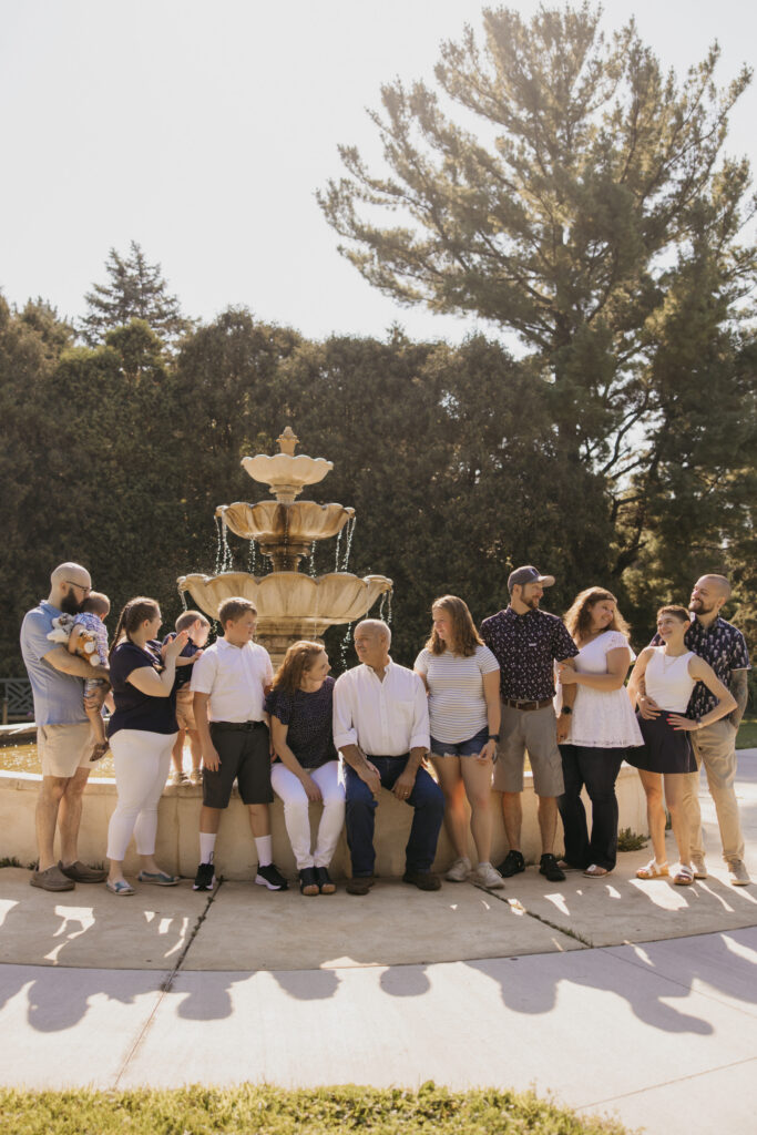 Full multigenerational family smiling together at a garden fountain during a family reunion photo session