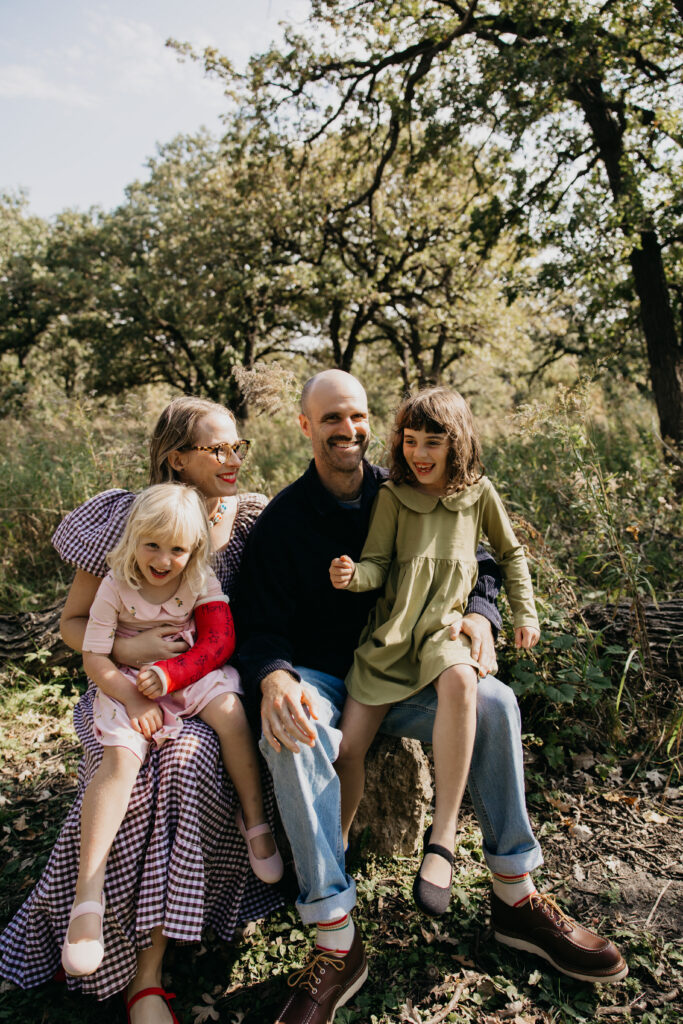 Family of four sitting together on a fallen log in the woods, laughing