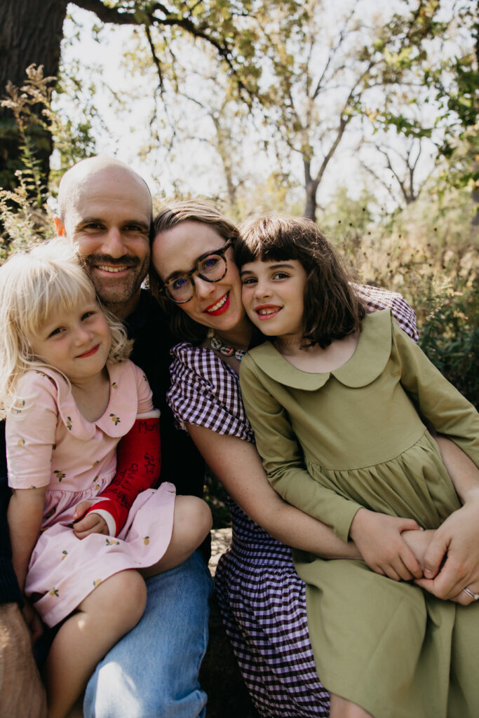 Close-up of dad, mom, and two daughters smiling together in the woods