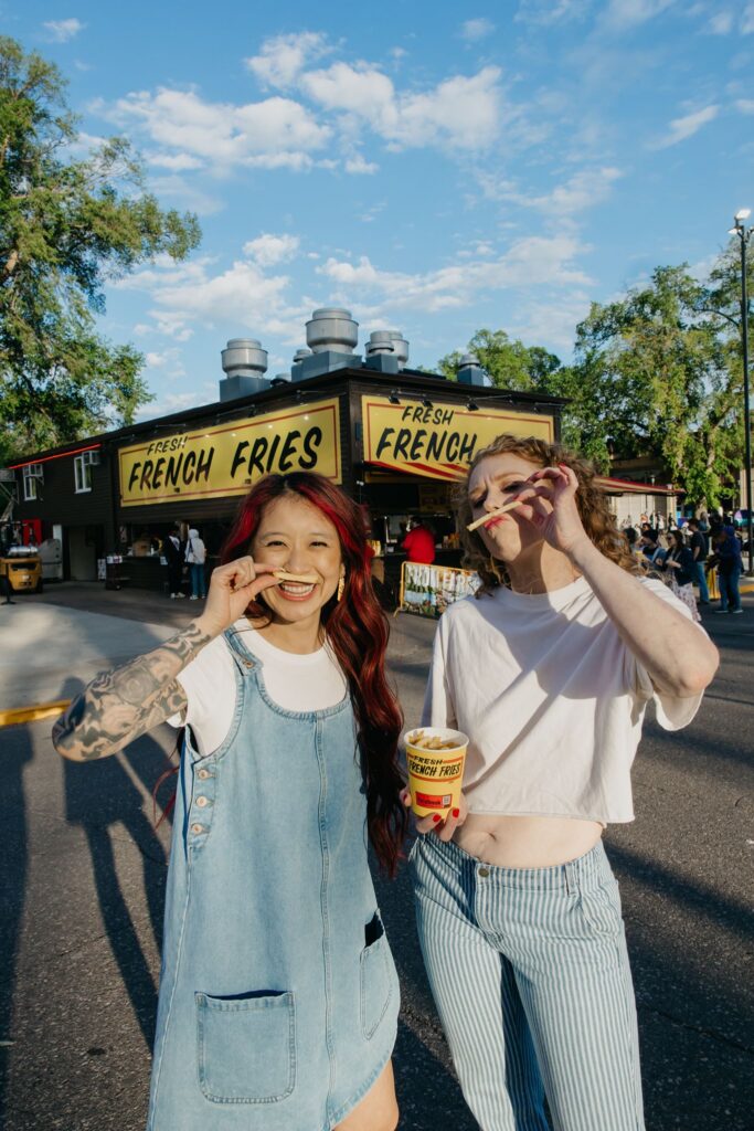Two women laughing with a cookie bucket in front of a French fries stand