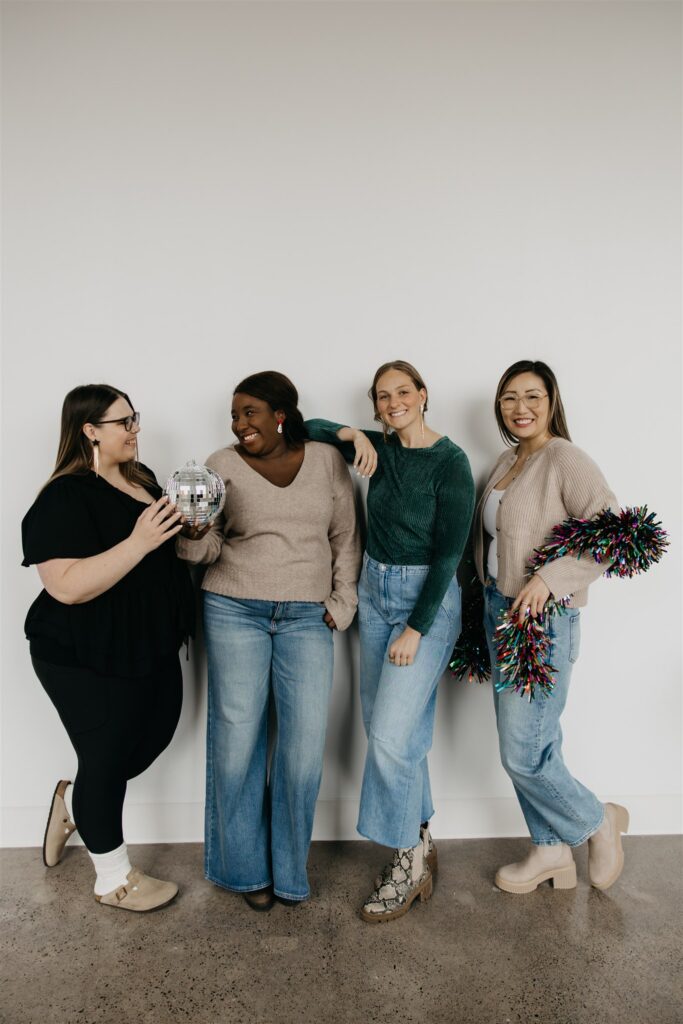 Four team members in neutral sweaters and denim posed together against a white backdrop