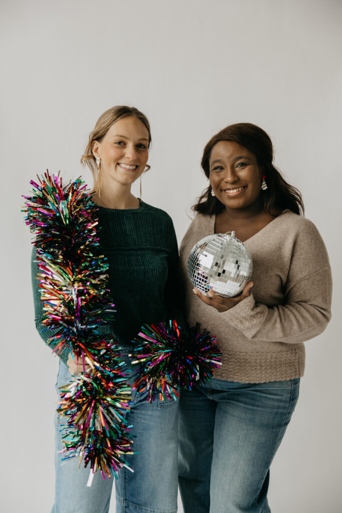 Two teammates laughing with rainbow tinsel and a disco ball during holiday team brand photography