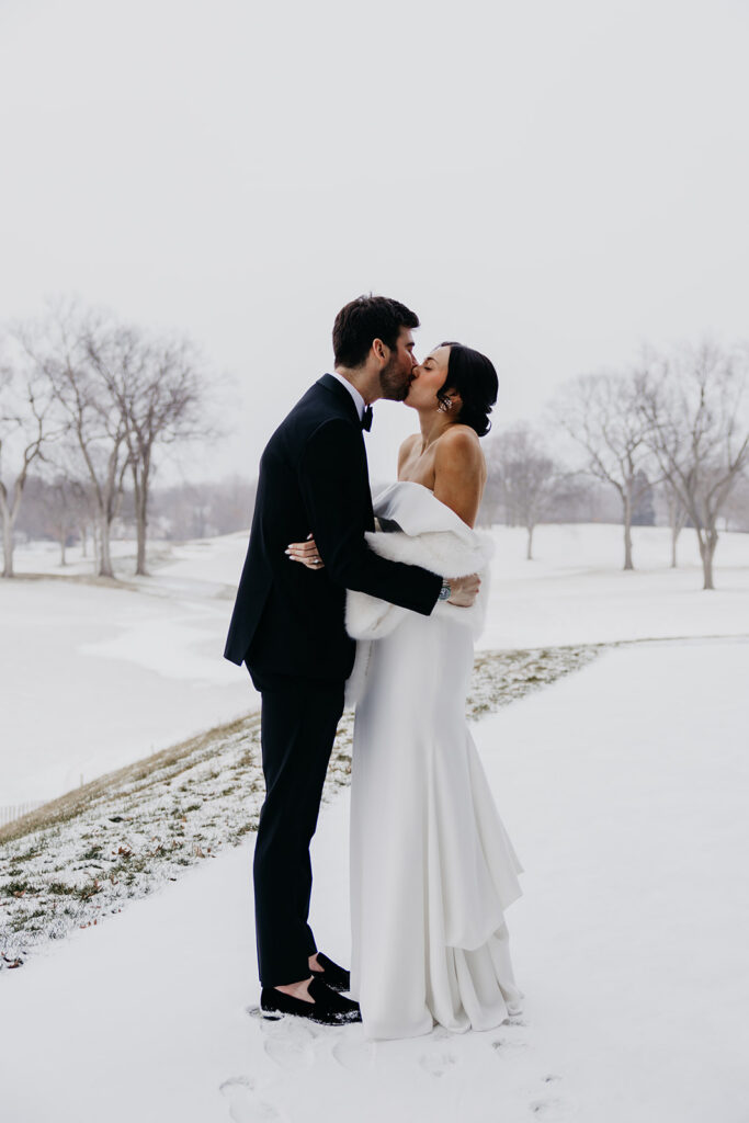 Groom lifting bride for a kiss during a snowy winter wedding portrait session