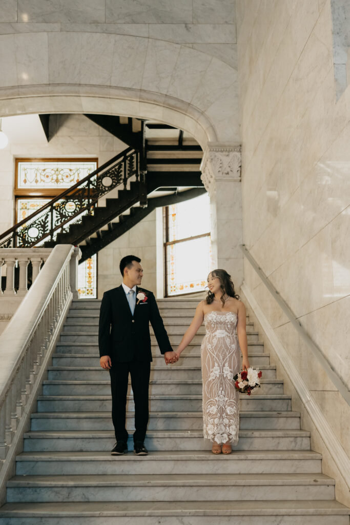 Bride and groom holding hands walking down a marble staircase inside the courthouse