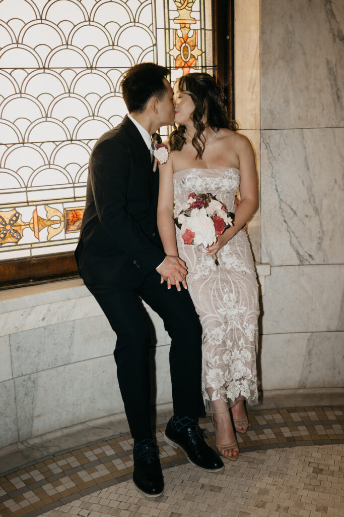 Bride and groom kissing near a stained glass window inside the courthouse