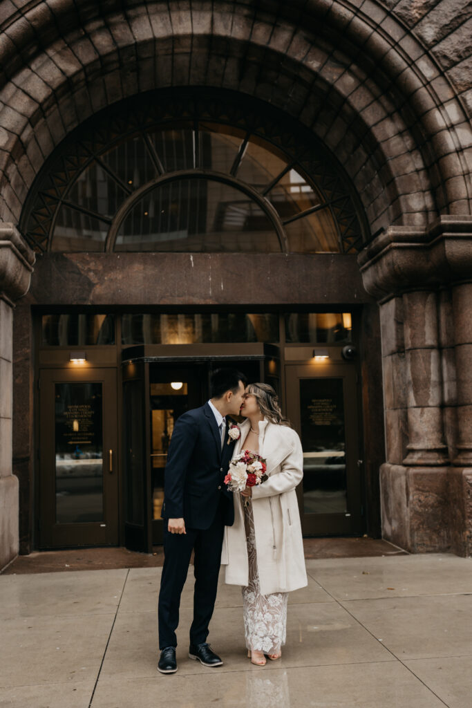 Bride and groom sharing a kiss outside a historic stone building entrance