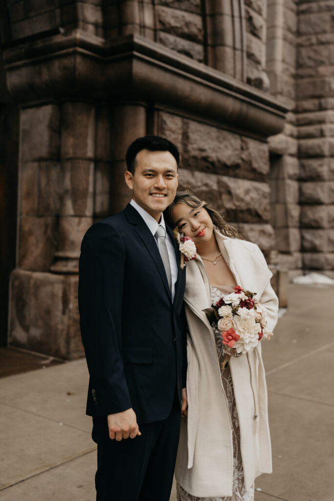 Bride and groom smiling together outside a stone courthouse exterior