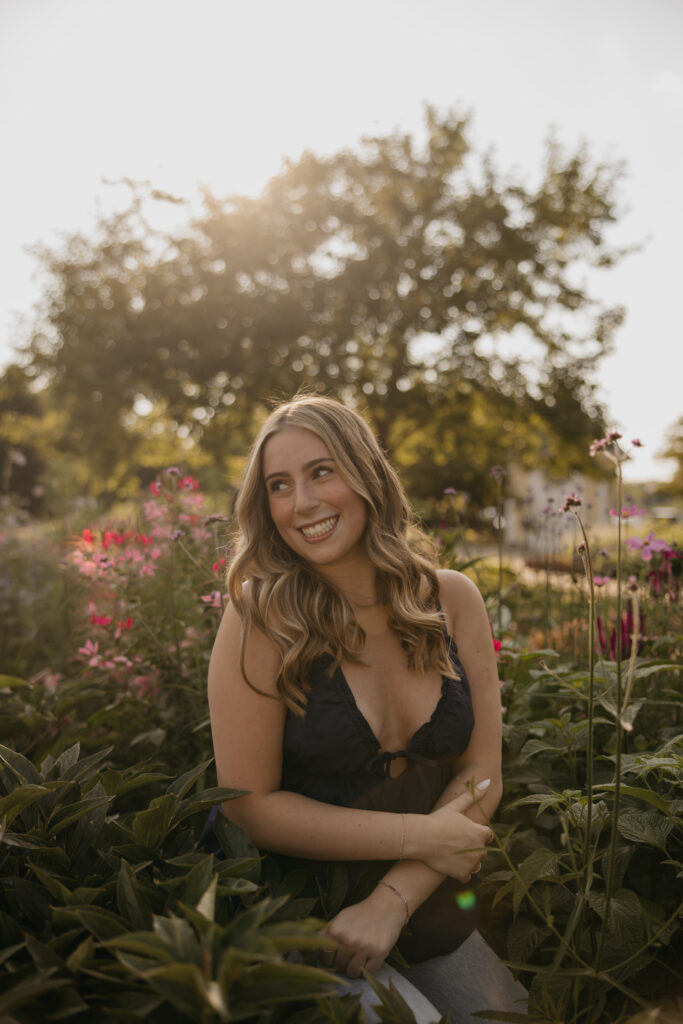 Laughing senior in a navy top among pink blooms during golden-hour garden senior pictures
