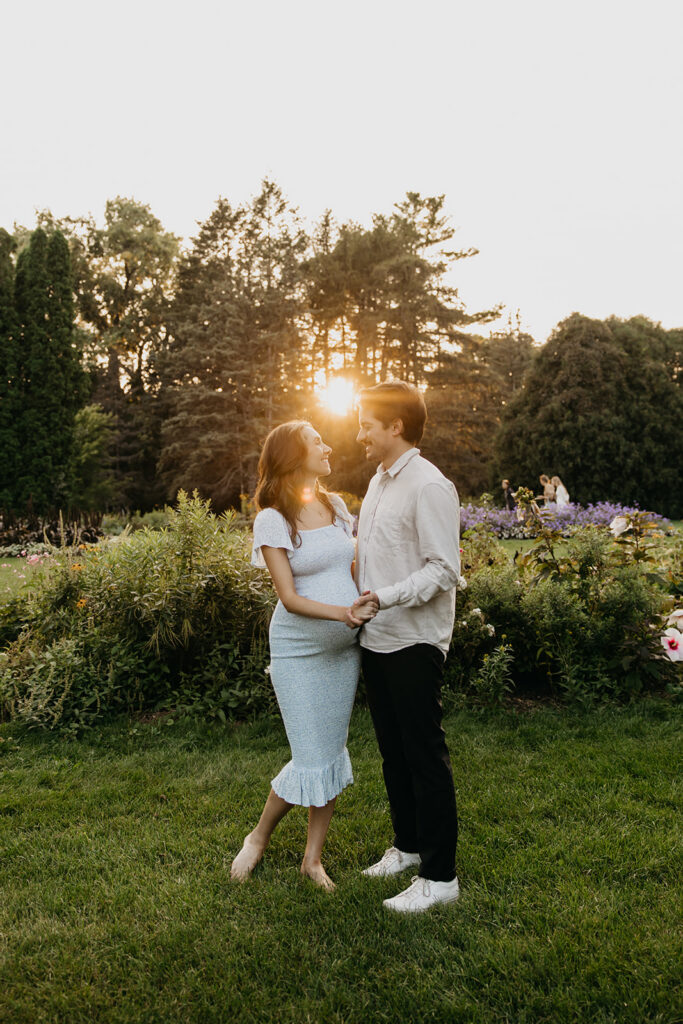 Pregnant couple standing together on a garden path lit by setting sun
