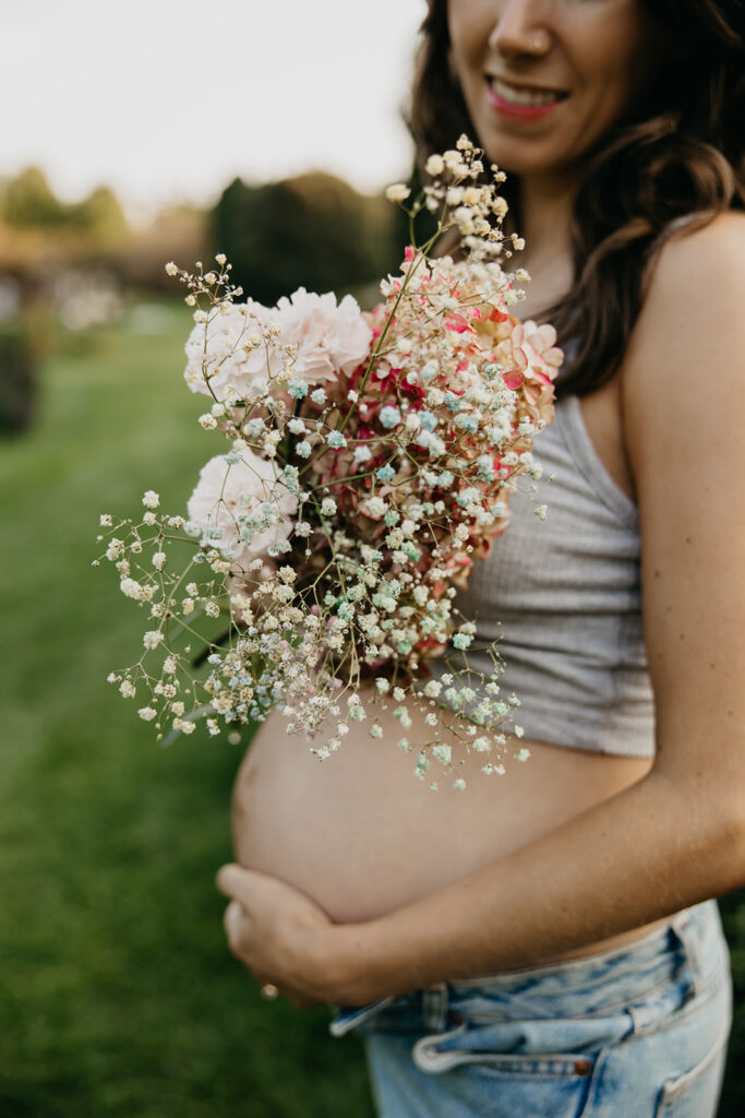 Pregnant woman holding a baby's breath and rose bouquet against her belly