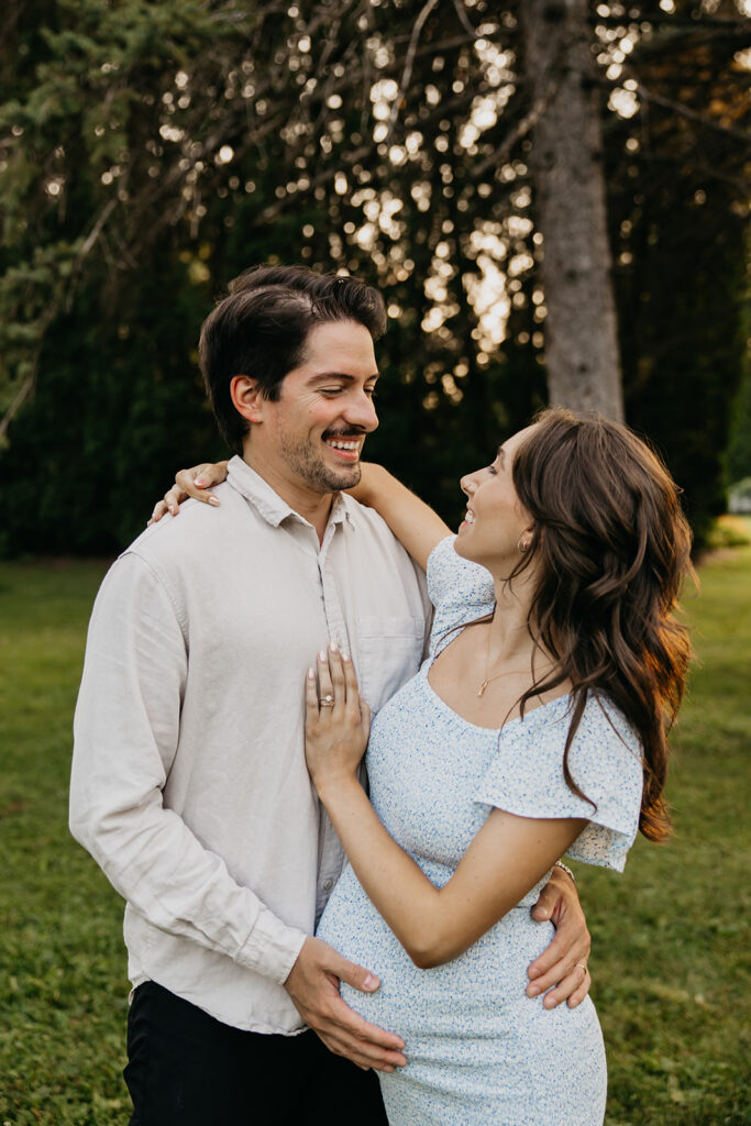 Smiling couple embracing outdoors, his hand resting on her pregnant belly