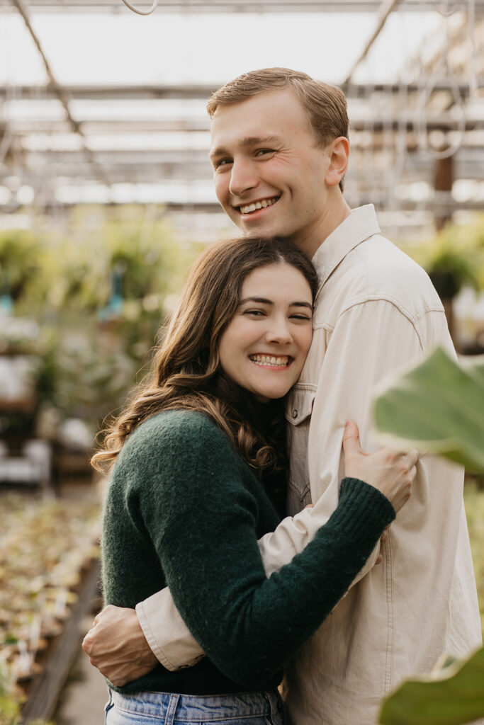 Close portrait of a smiling couple hugging among green leaves in a greenhouse
