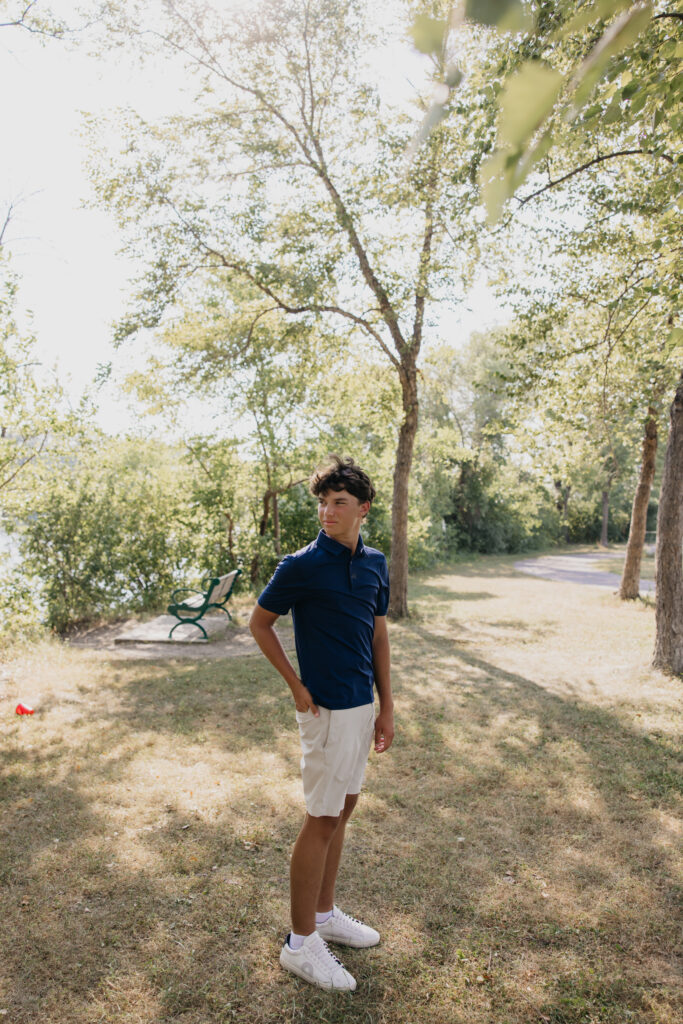 Senior guy in a navy polo standing on a shaded park path near the river