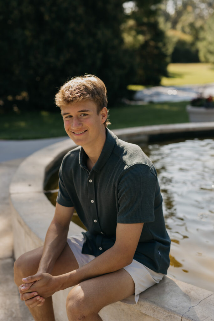 Senior guy sitting at the edge of a stone fountain in a green button-up shirt