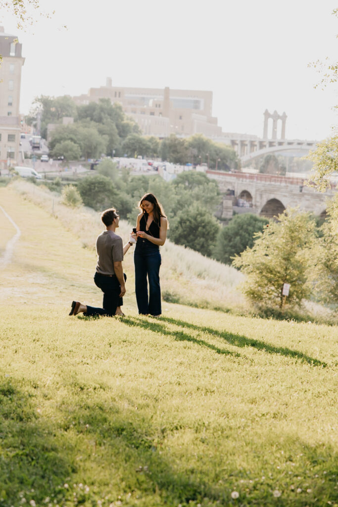 Man kneeling on one knee proposing to his partner on a Minneapolis hillside