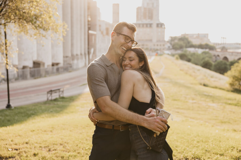 Engaged couple laughing and embracing in front of the Mill City grain silos in Minneapolis at golden hour