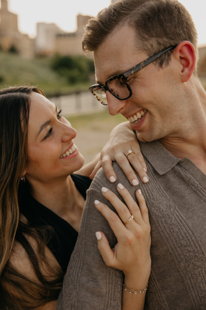 Newly engaged couple laughing with her hand and ring resting on his shoulder in Minneapolis