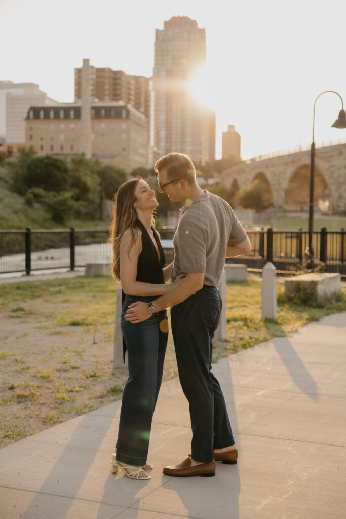 Engaged couple facing each other outdoors in Minneapolis with the skyline behind them