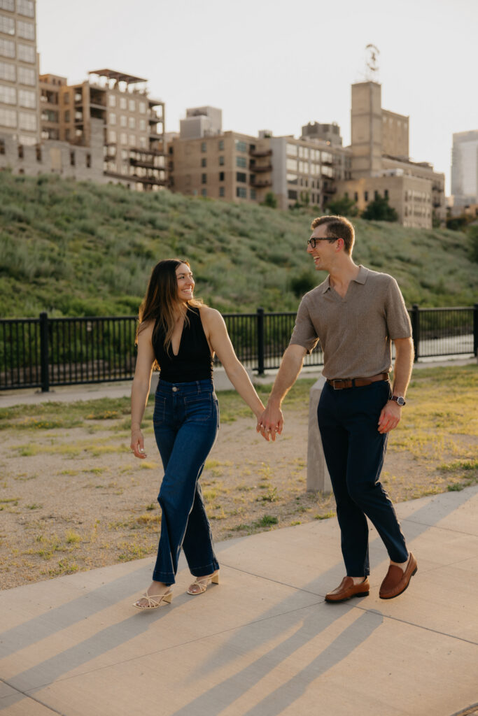 Engaged couple walking hand in hand along a Minneapolis path at golden hour