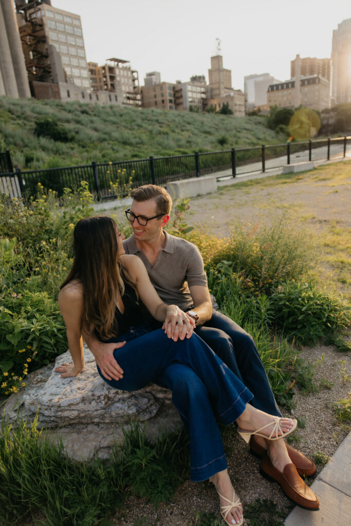 Engaged couple sitting together and laughing on a rock in Minneapolis