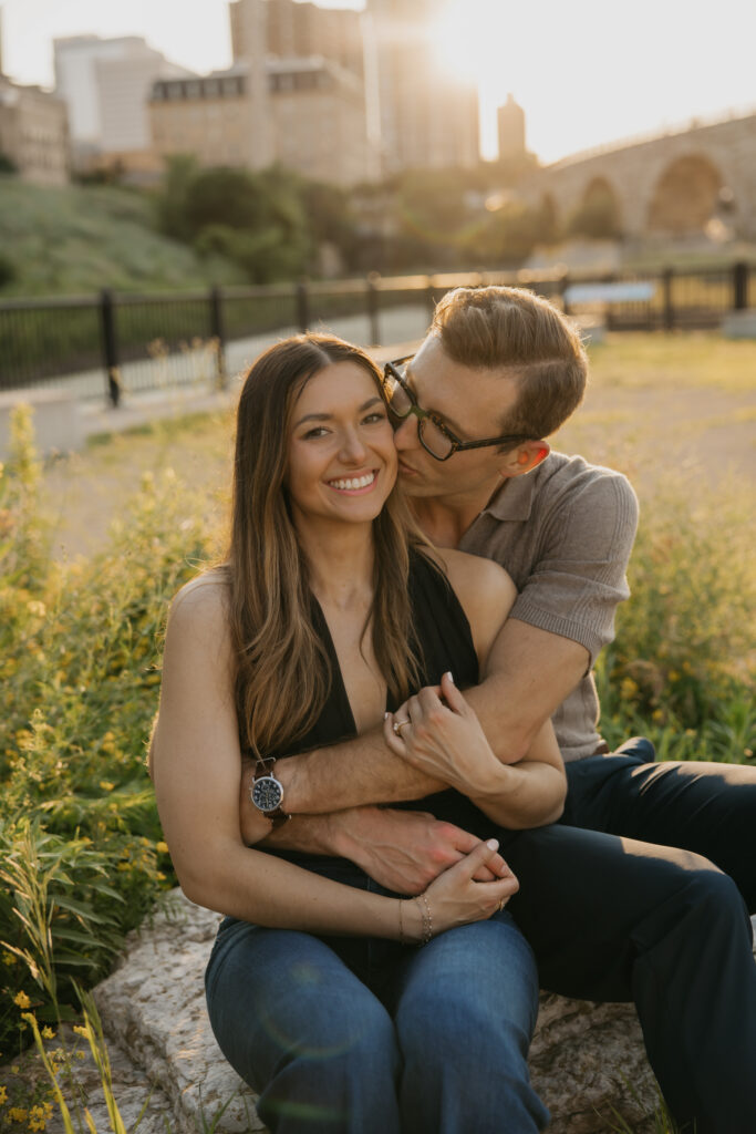 Engaged couple laughing and embracing outdoors in Minneapolis with the skyline behind them