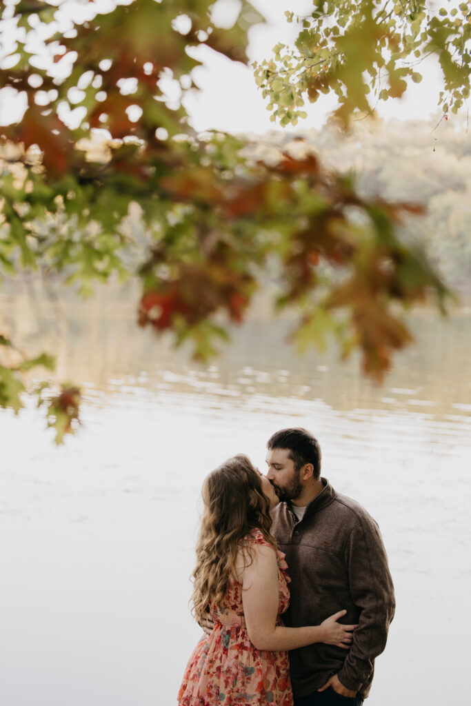 Couple kissing under a canopy of red and gold fall leaves near a lake in Minneapolis