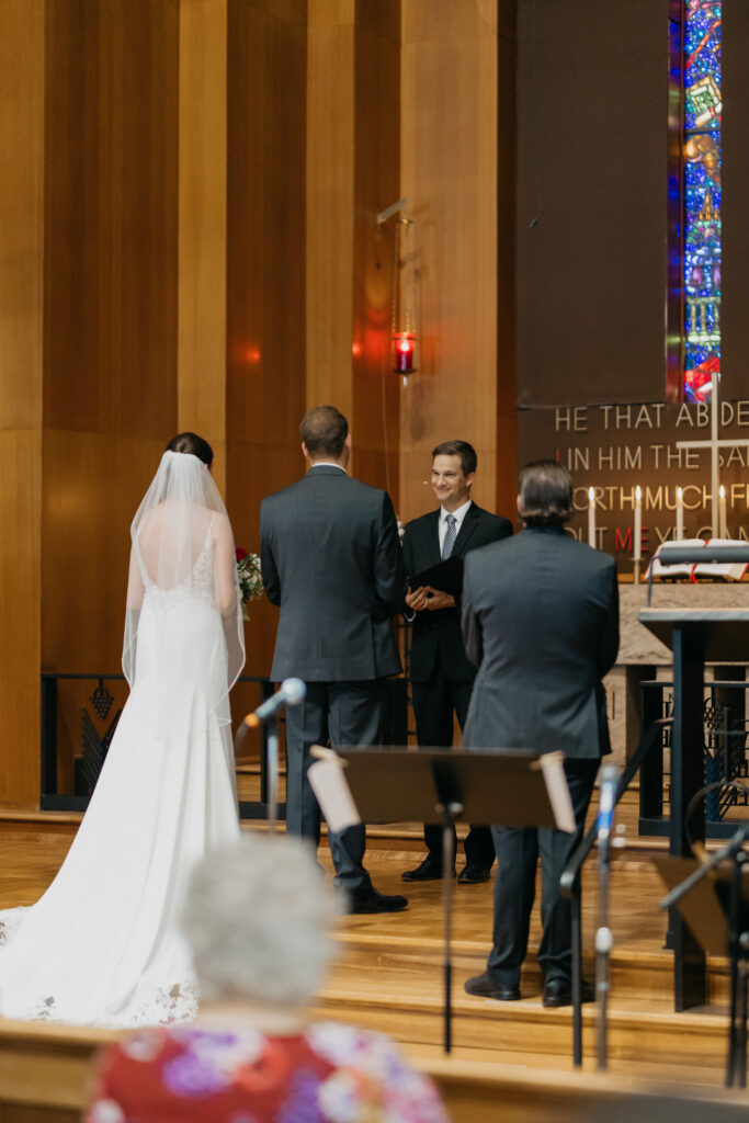 Bride and groom face the officiant at the altar, grandmother seated in the foreground