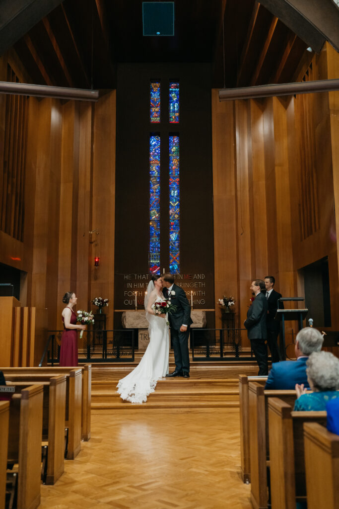 Bride and groom exchange vows at the altar with the wedding party standing nearby