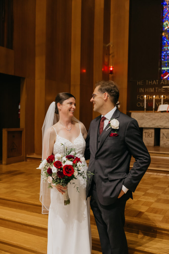 Bride and groom laugh together at the altar beneath the stained glass window