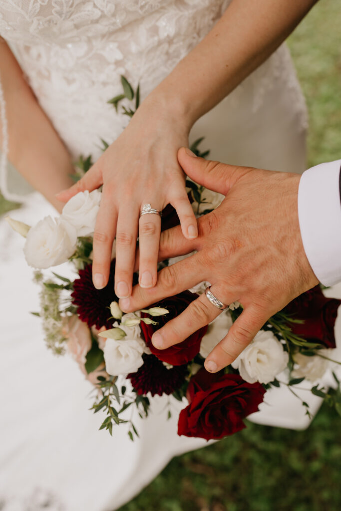 Close-up of bride and groom's joined hands resting on the bouquet, wedding rings visible