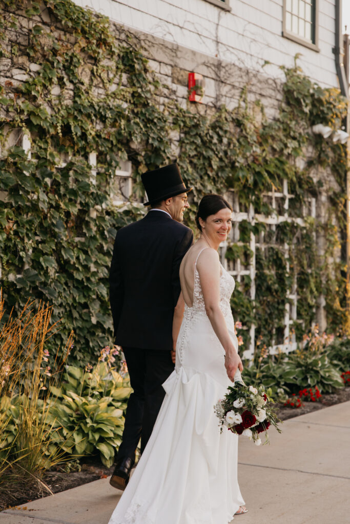 Bride and groom walk hand in hand along the ivy-covered wall at Keller Golf Course